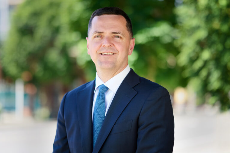 Luke Parker in a navy suit and blue tie, photographed outdoors